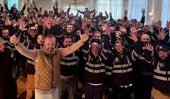 Group of people wearing black urture jackets with raised hands in a large room.