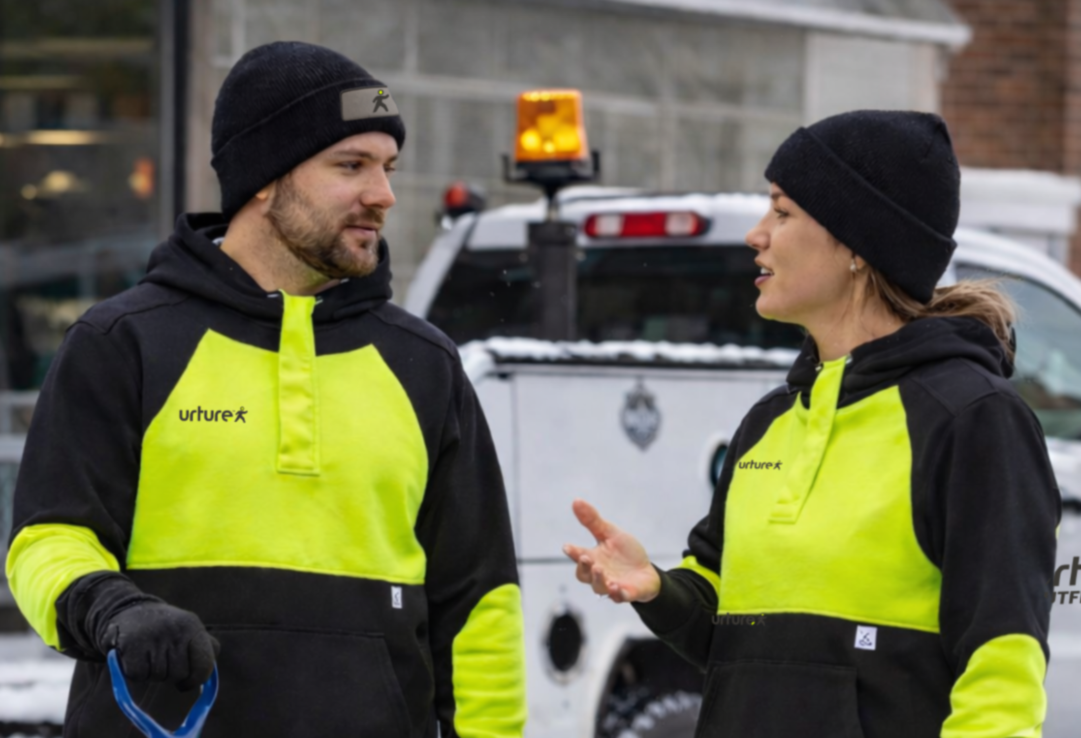 Two people wearing high-visibility jackets standing in front of a work truck.